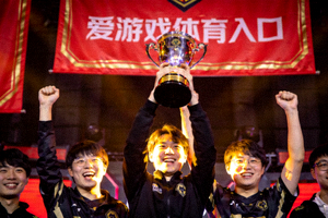 战队举起冠军奖杯庆祝，背景有爱游戏体育入口赞助横幅